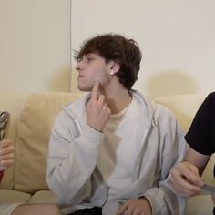 two young men sitting on a couch talking to each other while holding utensils