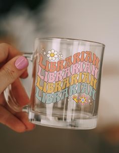 a person holding a glass with the words librarian written on it in different colors and designs