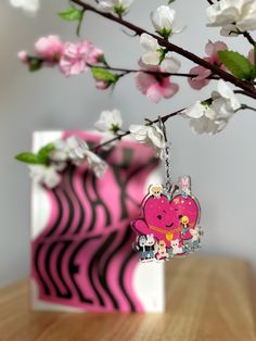 a pink heart shaped keychain sitting on top of a wooden table next to flowers