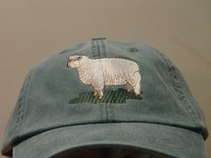 a green hat with a white sheep embroidered on the front and side, sitting against a wall