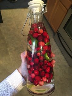 a person holding a glass bottle filled with water and cranberries