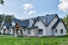 a large white house with metal roofing and blue shingles on the windows, surrounded by lush green grass