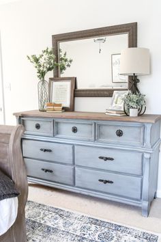 a blue dresser sitting in front of a mirror on top of a wooden dresser next to a bed