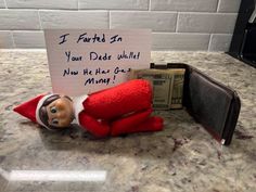 an elf is laying on the counter next to a note that says i farted in your dad's wallet