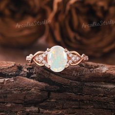 a white opal and diamond ring sitting on top of a piece of drift wood