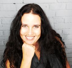 a woman with long black hair is smiling for the camera while sitting in front of a brick wall