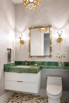 a white toilet sitting next to a bathroom sink under a golden mirror above a green counter top