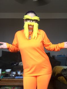 a woman in an orange outfit with her hands out to the side, wearing large yellow wig and glasses