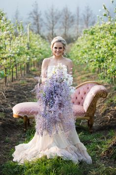 a woman in a wedding dress holding a bouquet of purple flowers sitting on a bench