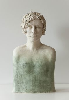 a statue of a woman with flowers in her hair is sitting on a table next to a white wall