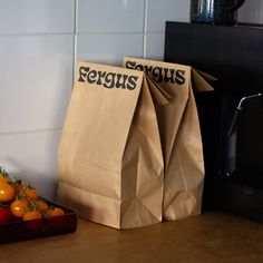 two brown paper bags sitting on top of a counter next to oranges and a microwave