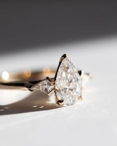 an engagement ring with two pear shaped diamonds on it's side, sitting on a white surface