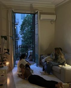 two women sitting on couches in a living room with an open door to the outside