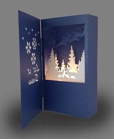 an open book with paper cut trees and snowflakes on the pages, which are lit up at night