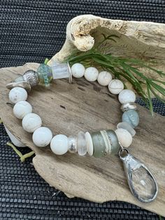 This unique "Boho Chic: Handcrafted Cream Howlite, Raw Quartz, African Recycled Glass, Aquamarine, and Lampwork Beaded Bracelet with Antiqued Silver Accents and Crystal Pendant" is a stunning blend of natural gemstones and mixed beads, creating a one-of-a-kind piece that complements any outfit. The antiqued silver accents and crystal pendant add a touch of elegance, making it a perfect accessory for any occasion. Each bead is carefully selected and handcrafted with attention to detail, ensuring Bohemian White Bracelets With Gemstone Beads, Bohemian White Beaded Bracelets With Natural Stones, White Bohemian Beaded Bracelets For Healing, Chic Bracelet, Raw Quartz, Silver Accents, Recycled Glass, Lampwork Beads, Crystal Pendant