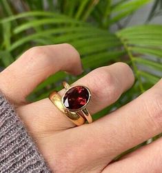 a woman's hand wearing a gold ring with a garnet colored stone on it