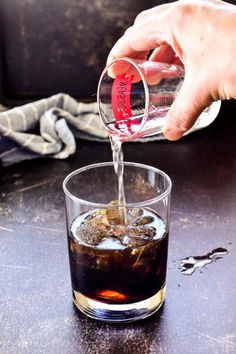 someone is pouring something into a glass on the table with ice and water in it