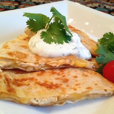 two quesadillas on a white plate topped with sour cream and cilantro