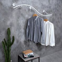 an ironing board with clothes hanging on it and a cactus next to it in front of a grey wall