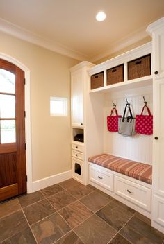 a mud room with white cabinets and baskets on the wall, two bags hanging from hooks