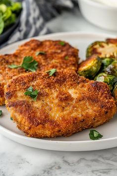 three pieces of fried chicken on a plate with brussel sprouts