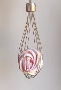 a pink rose is hanging from a metal wire light fixture with a white wall in the background