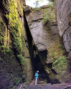 a person standing in the middle of a narrow ravine between two large rocks with moss growing on them