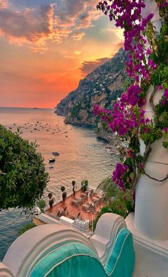 the sun is setting over an ocean with boats in the water and purple flowers growing on it