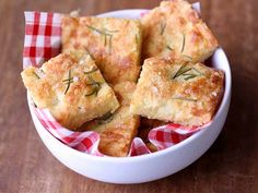 some food in a white bowl on a wooden table with a red and white checkered napkin