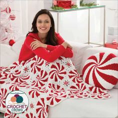 a woman sitting on a couch with a red and white crochet blanket