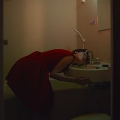 a woman in a red dress is leaning over a sink with her head on the faucet