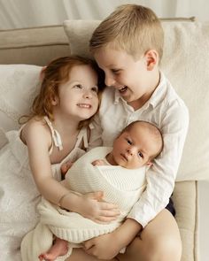 two young children cuddle together on a couch with their arms around the baby's head