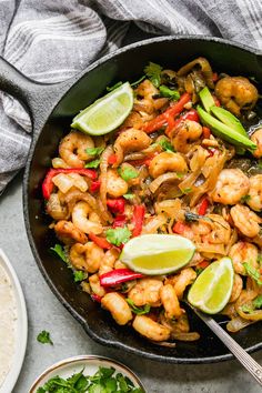 a skillet filled with shrimp and vegetables next to tortillas, lime wedges and cilantro