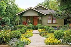 a green house with lots of flowers and bushes around it's front yard area