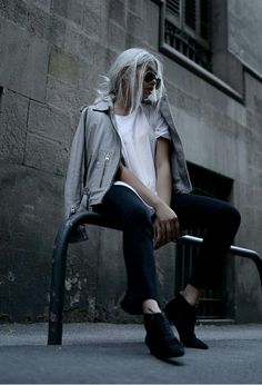 a woman with white hair sitting on a bench in front of a building wearing black shoes