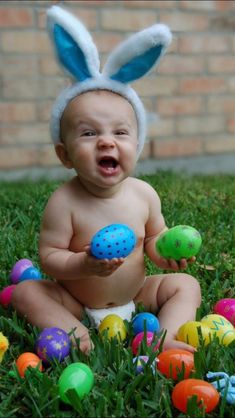 a baby sitting in the grass with an easter egg and bunny ears on it's head