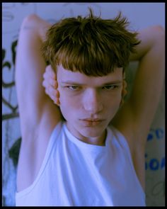 a young man with short brown hair is posing for the camera while wearing a white tank top