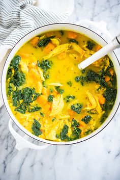 a white pot filled with yellow soup and spinach on top of a marble counter