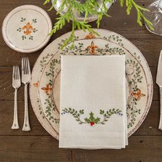 the place setting is set with white linens, silverware and holly - leaf napkins