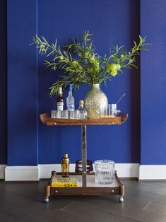 a bar cart with bottles and glasses on it in front of a wall painted blue