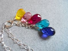 three different colored glass beads hanging from a silver chain on a gray surface with a white background