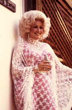 a woman in a pink and white dress leaning against a wall