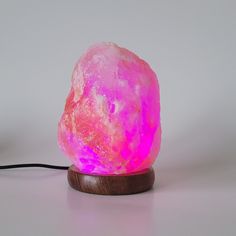 a pink himalayan rock lamp on a wooden base with a black cord attached to it