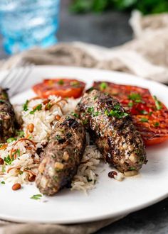 some meatballs and rice on a white plate with tomato wedges next to it