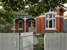 a white picket fence is in front of a red brick house with two large windows