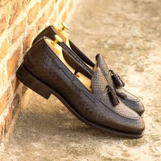 a pair of brown loafers with tassels on them leaning against a brick wall