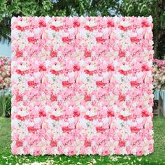 a large pink and white flowered quilt on the grass in front of some trees