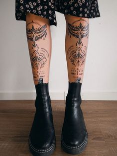 the legs and ankles of a woman with tattoos on her leg, wearing black rubber boots