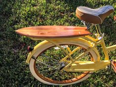 a yellow bicycle with a wooden seat and surfboard on it's back tire