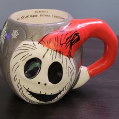 a ceramic mug with a face painted on the side and an orange handle is sitting on a table